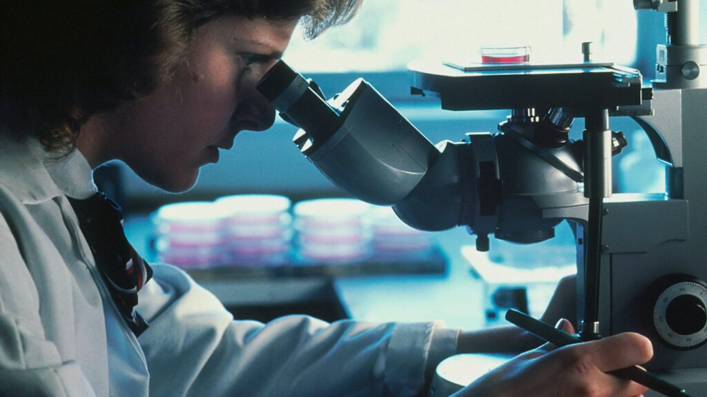 Scientist in a lab coat examining samples through a microscope in a Canadian research lab