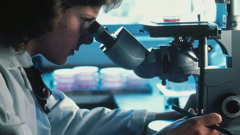 Scientist in a lab coat examining samples through a microscope in a Canadian research lab